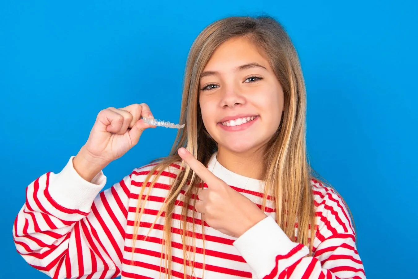 Smiling girl holding a clear aligner