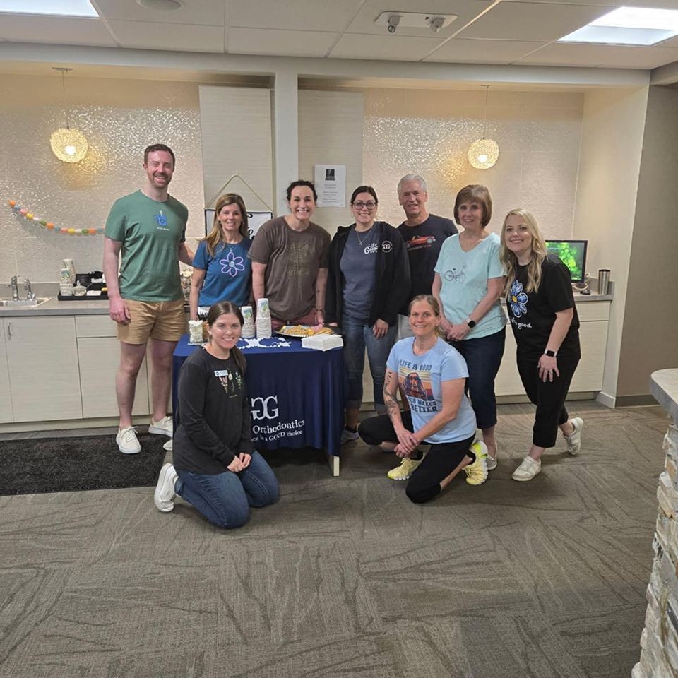 Group of orthodontic staff members posing and smiling around a table.