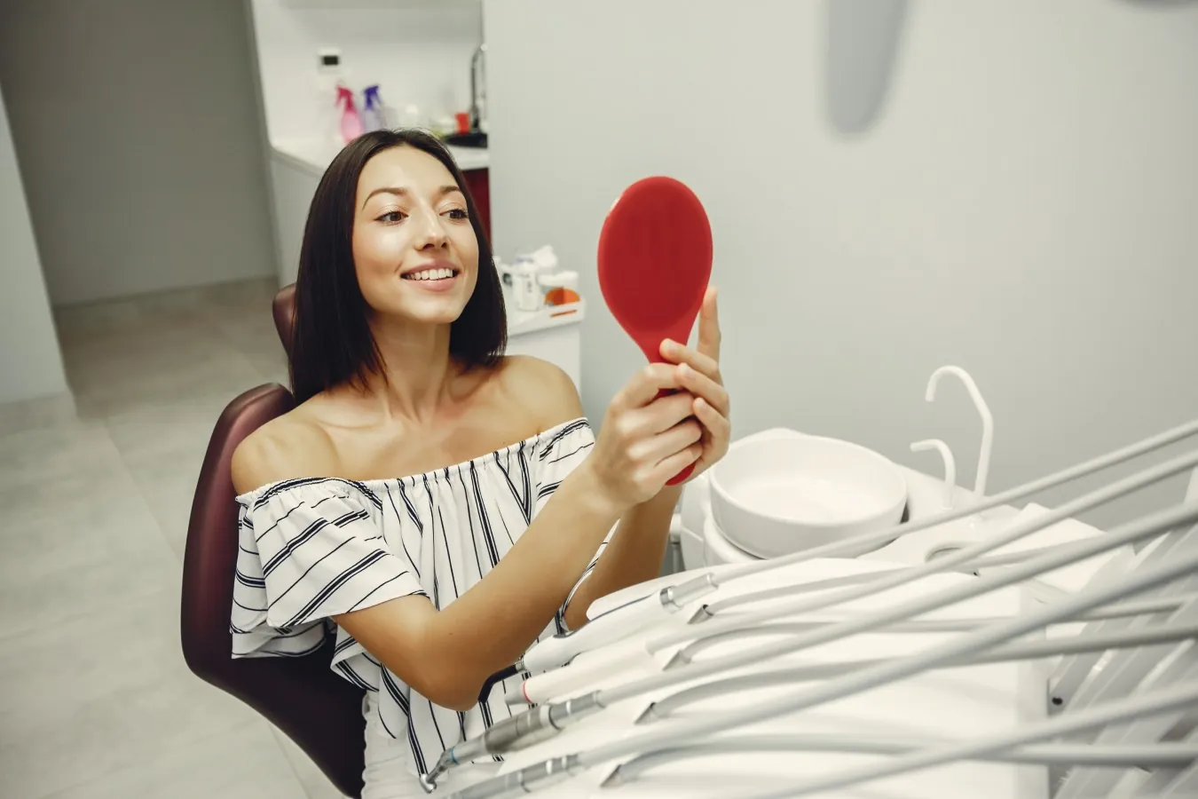 Young woman smiling at her teeth in a hand mirror